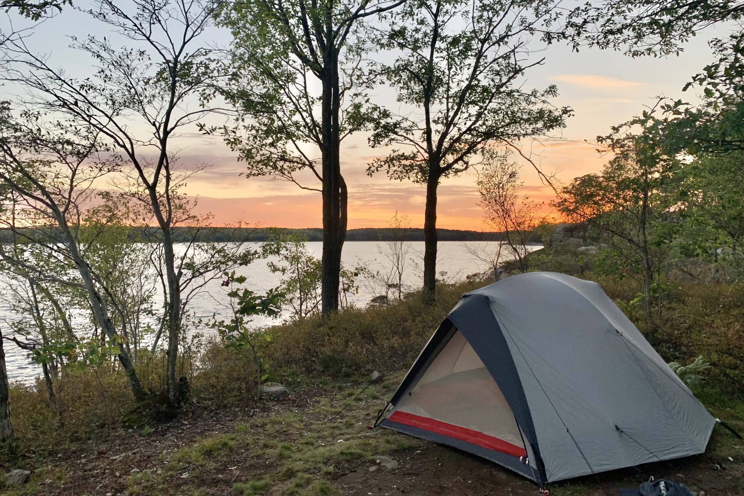 A grey tent nestled in trees with a sunset in the background